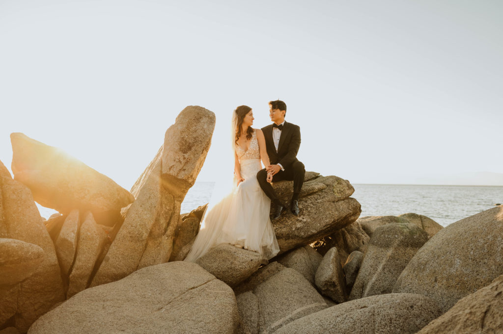 A couple in wedding attire sitting on rocks in Lake Tahoe, California.