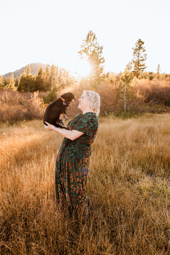 A woman holding her dog up for a photo at sunset.